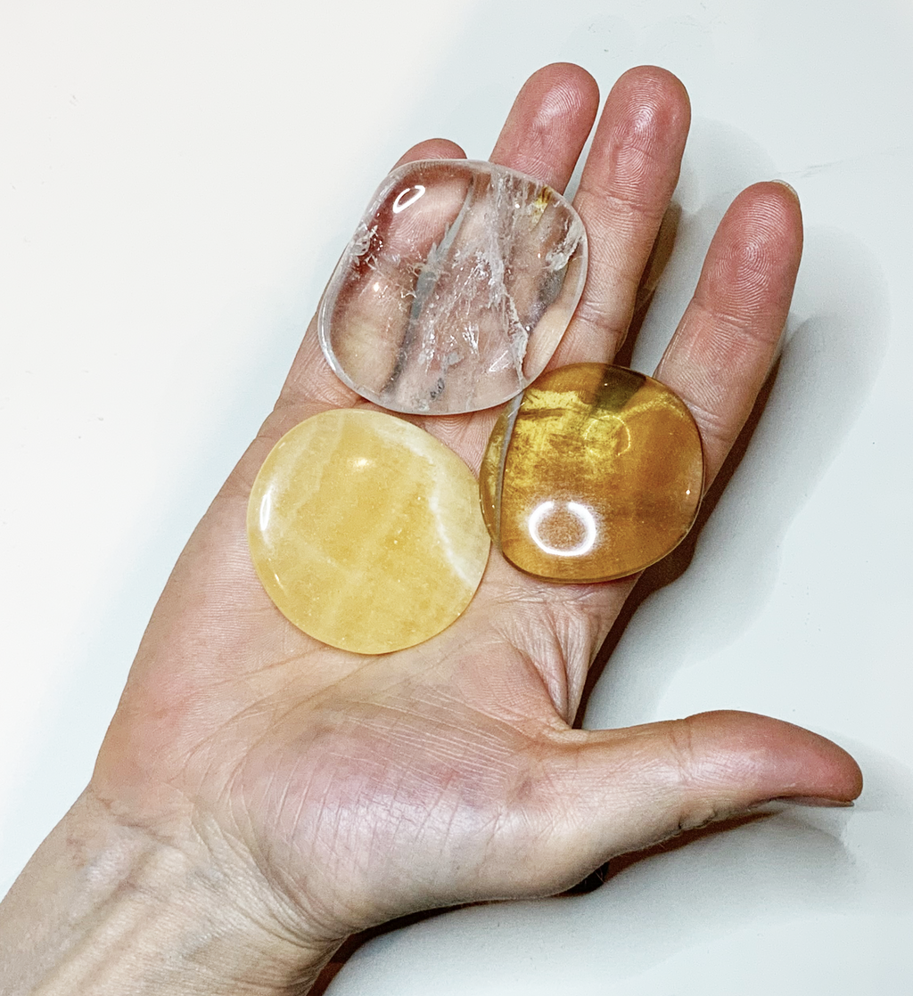Drei Scheibensteine Bergkristall, Orangencalcit, gelber Fluorit auf einer Hand liegend